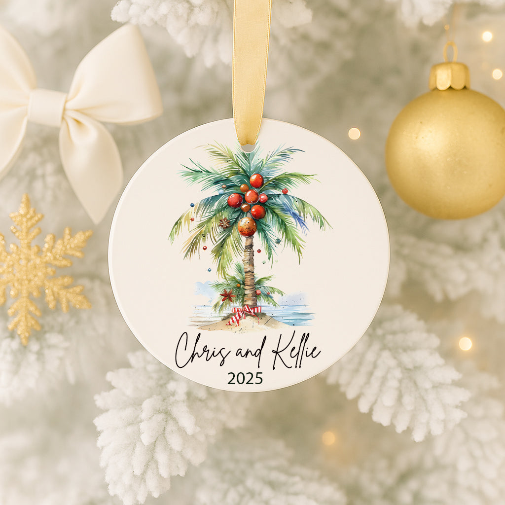 A round ornament hanging on a Christmas tree, featuring a palm tree with red and green ornaments and the names 'Chris' and 'Kelle' written on it.
