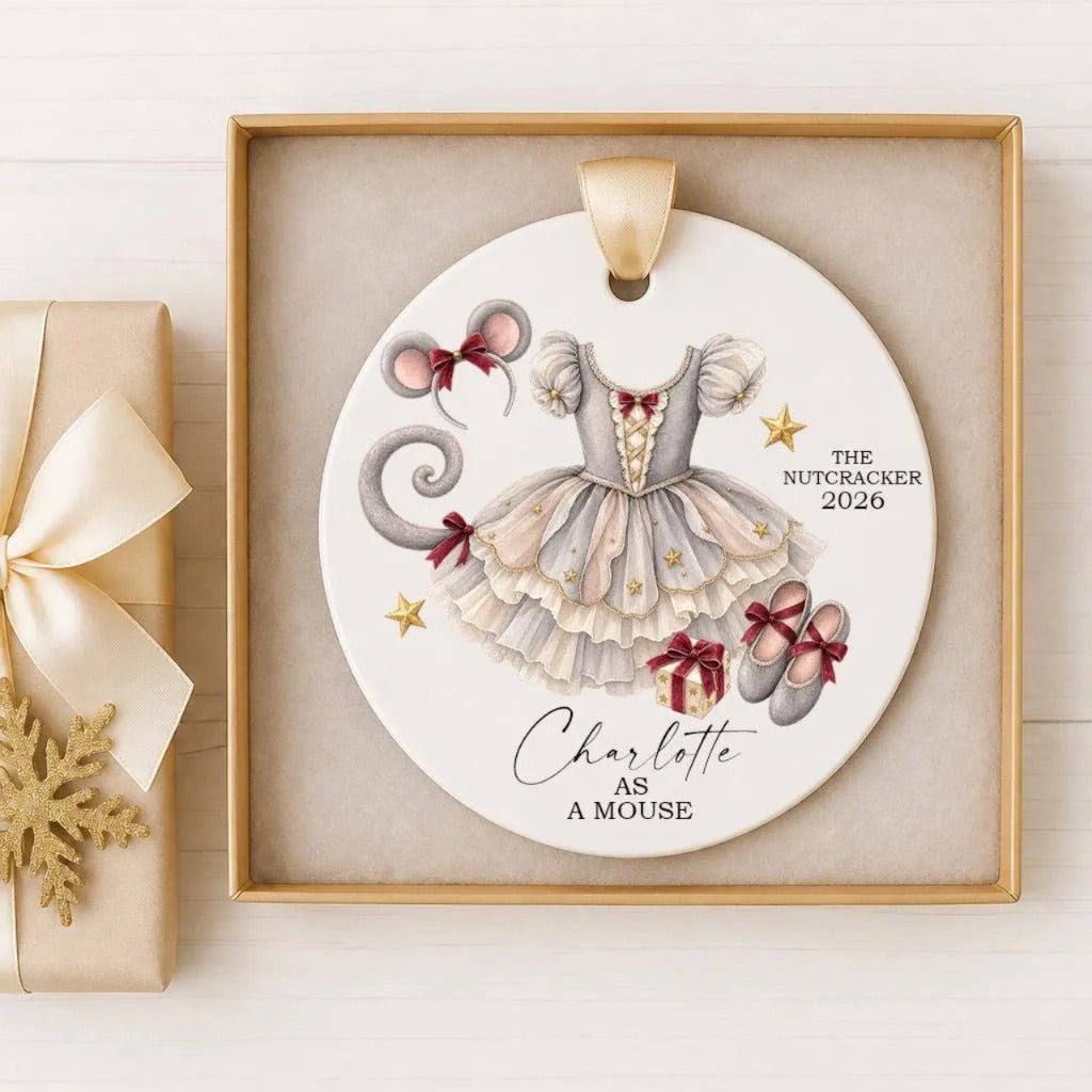 A decorative ornament featuring a white dress with a red bow, a pair of red shoes, and a gold star, along with the text "The Nutcracker 2026" and "Charlotte as a Mouse".