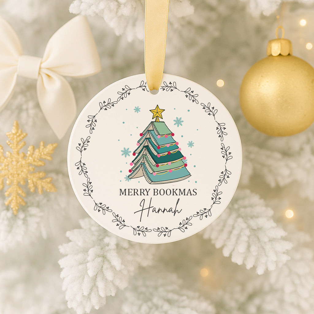A white Christmas tree ornament with a blue and green Christmas tree design, surrounded by a decorative border, and a gold ornament hanging nearby.