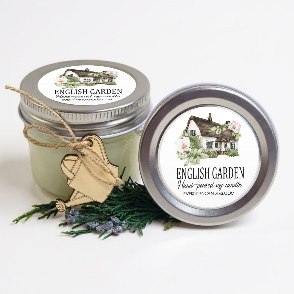 two jars of English Garden hand-poured soy candles, with a wooden watering can and greenery in the foreground.