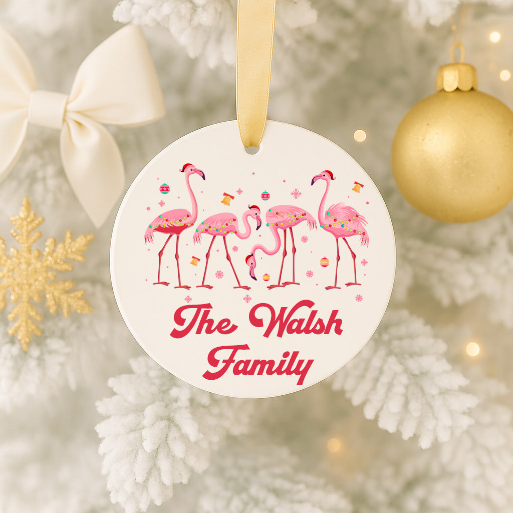 A white ornament with pink flamingos and the text "The Walsh Family" is hanging on a Christmas tree.