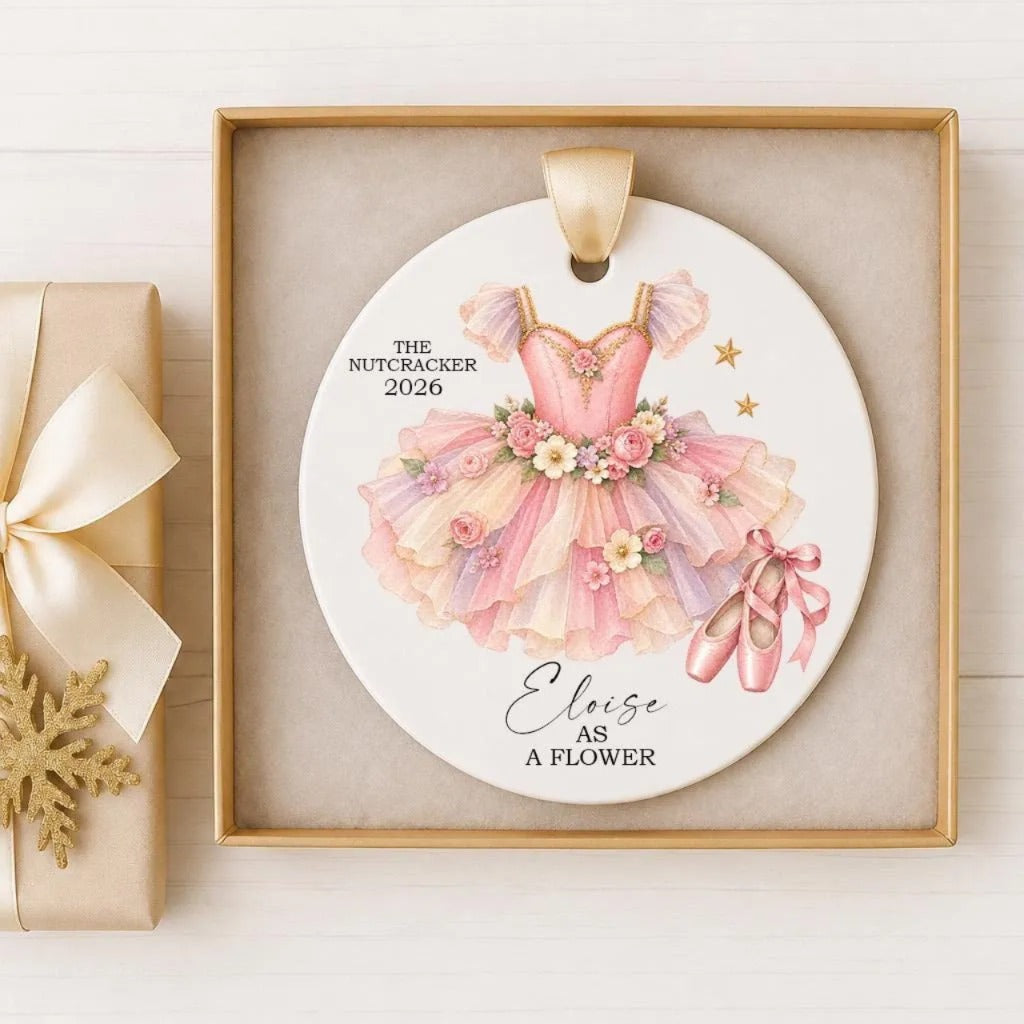 A decorative ornament featuring a pink tutu with flowers and ballet slippers, placed in a gold frame.