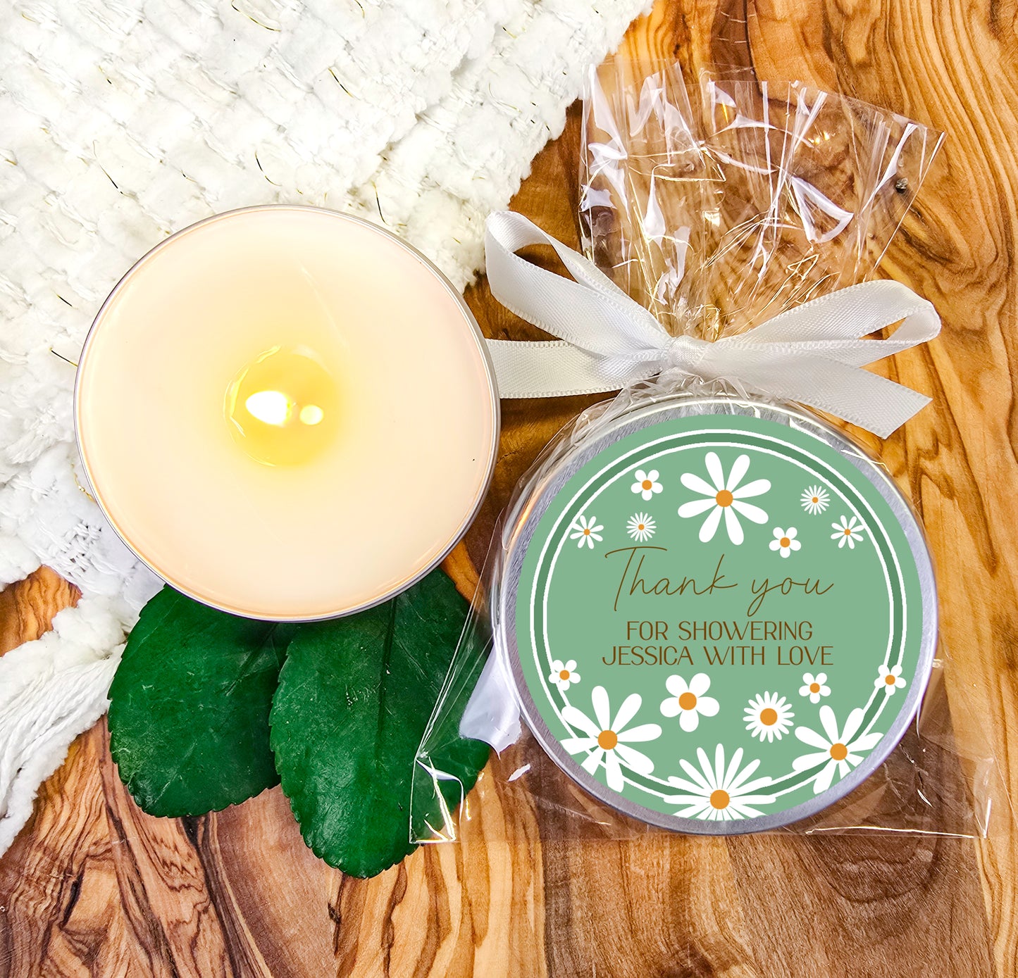 a white candle and some green leaves on a table