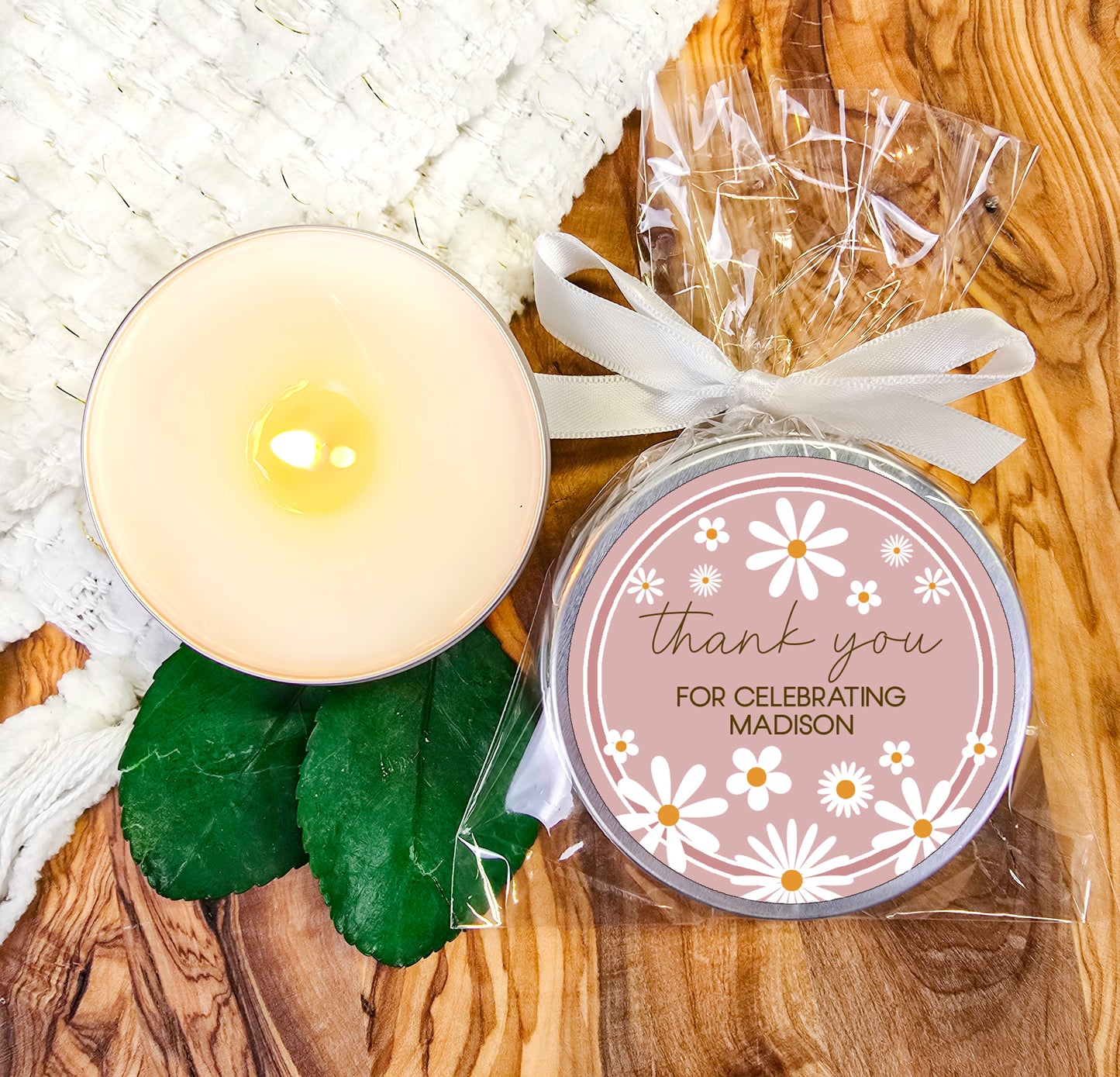 a white candle and some green leaves on a table