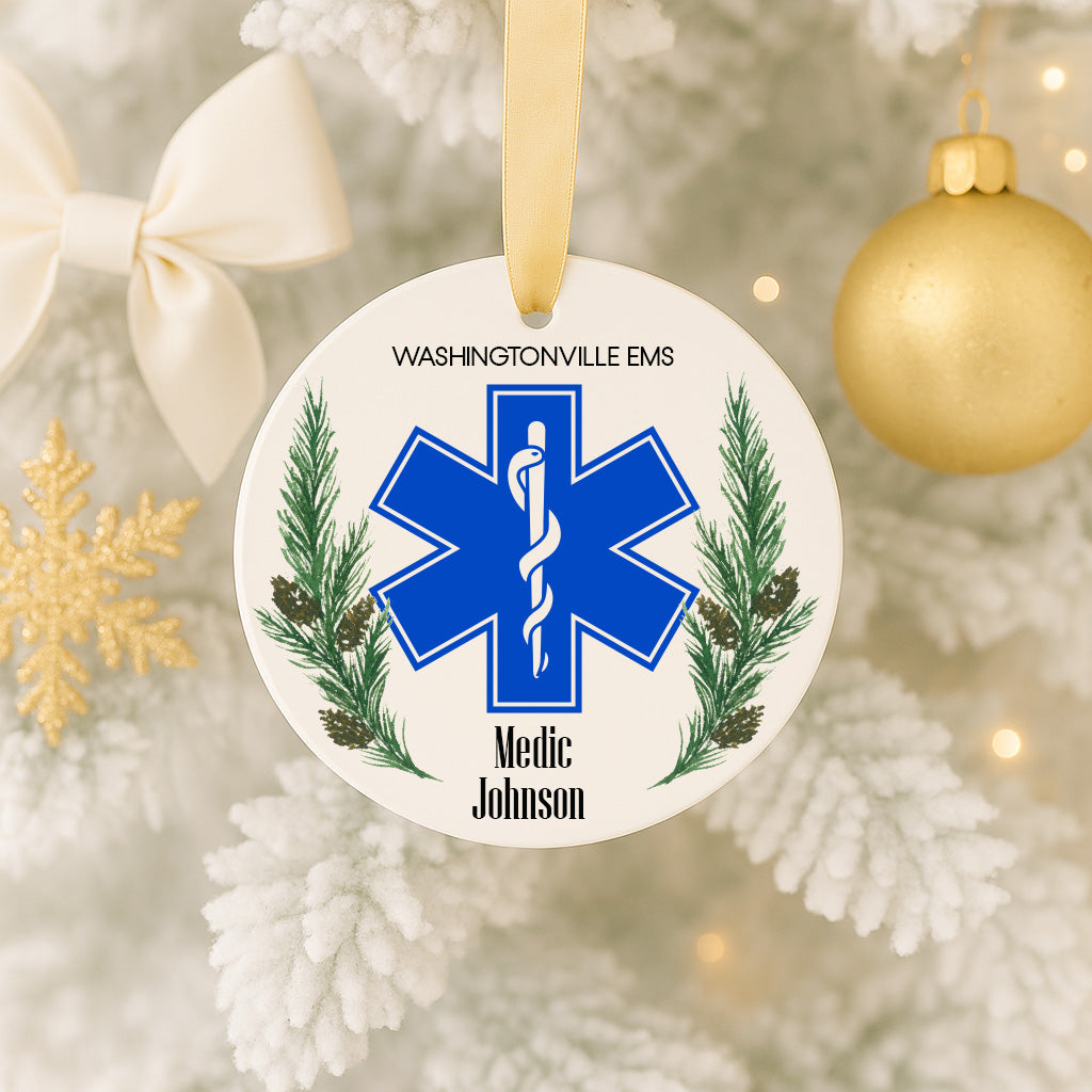 A white ornament with a blue star-shaped symbol and medical symbol, hanging on a Christmas tree.