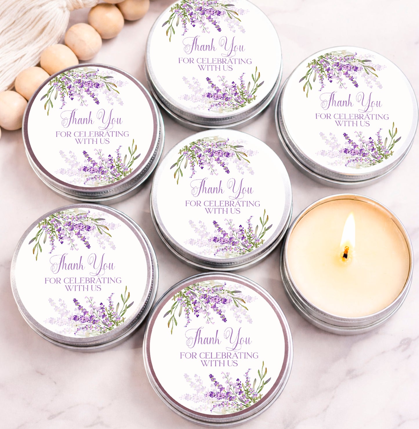 Lavender floral candle favors in silver tins with purple “Thank You for Celebrating With Us” labels, arranged on table for bridal shower or wedding.