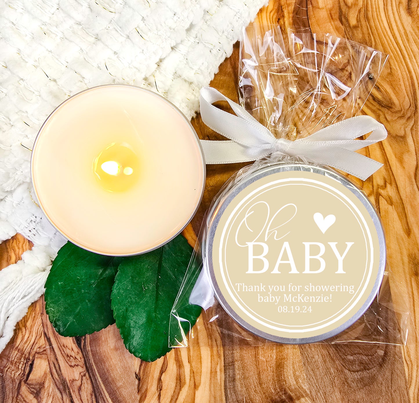 a white candle and some green leaves on a wooden table