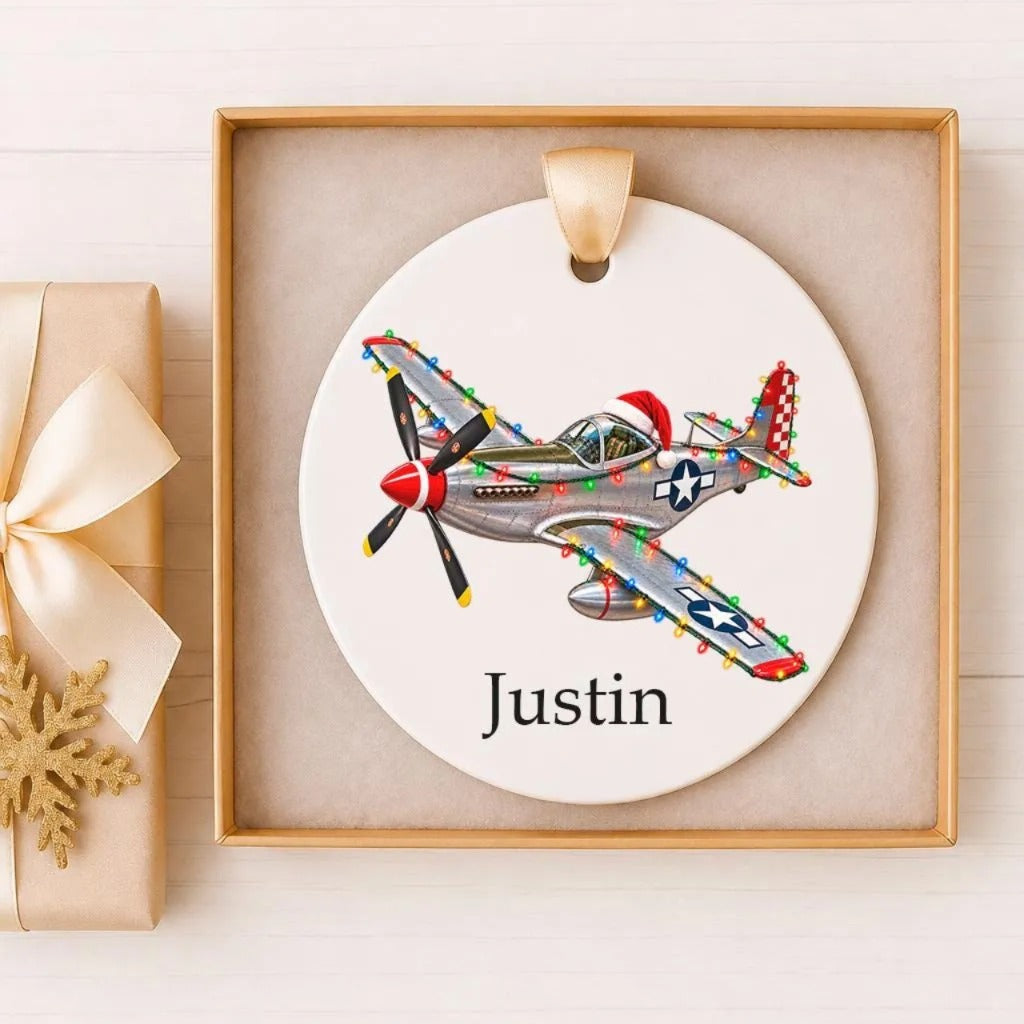 A white ceramic ornament with a picture of a vintage fighter plane, possibly a P-51 Mustang, and the name "Justin" written on it. The ornament is displayed in a wooden frame.