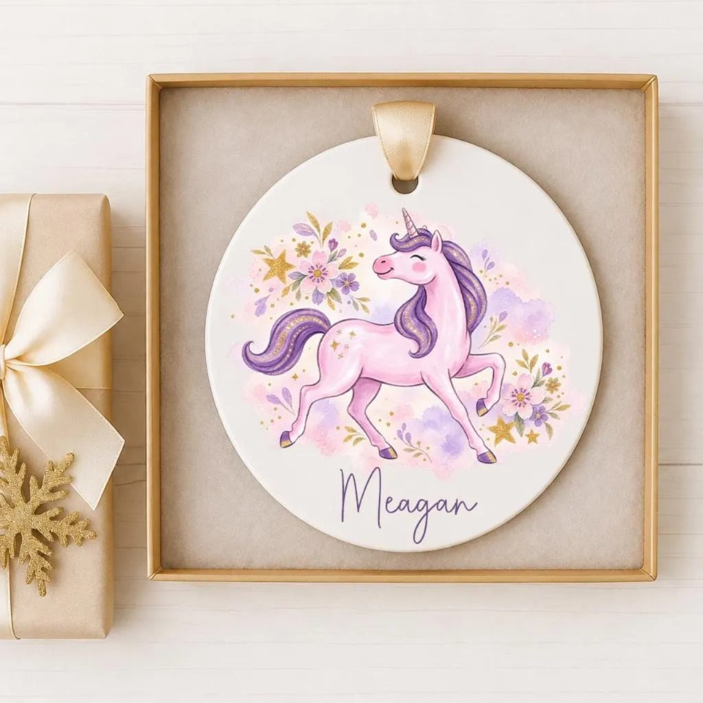 A round ceramic ornament featuring a pink unicorn with purple mane and tail, surrounded by colorful flowers and the name "Megan" written on it.