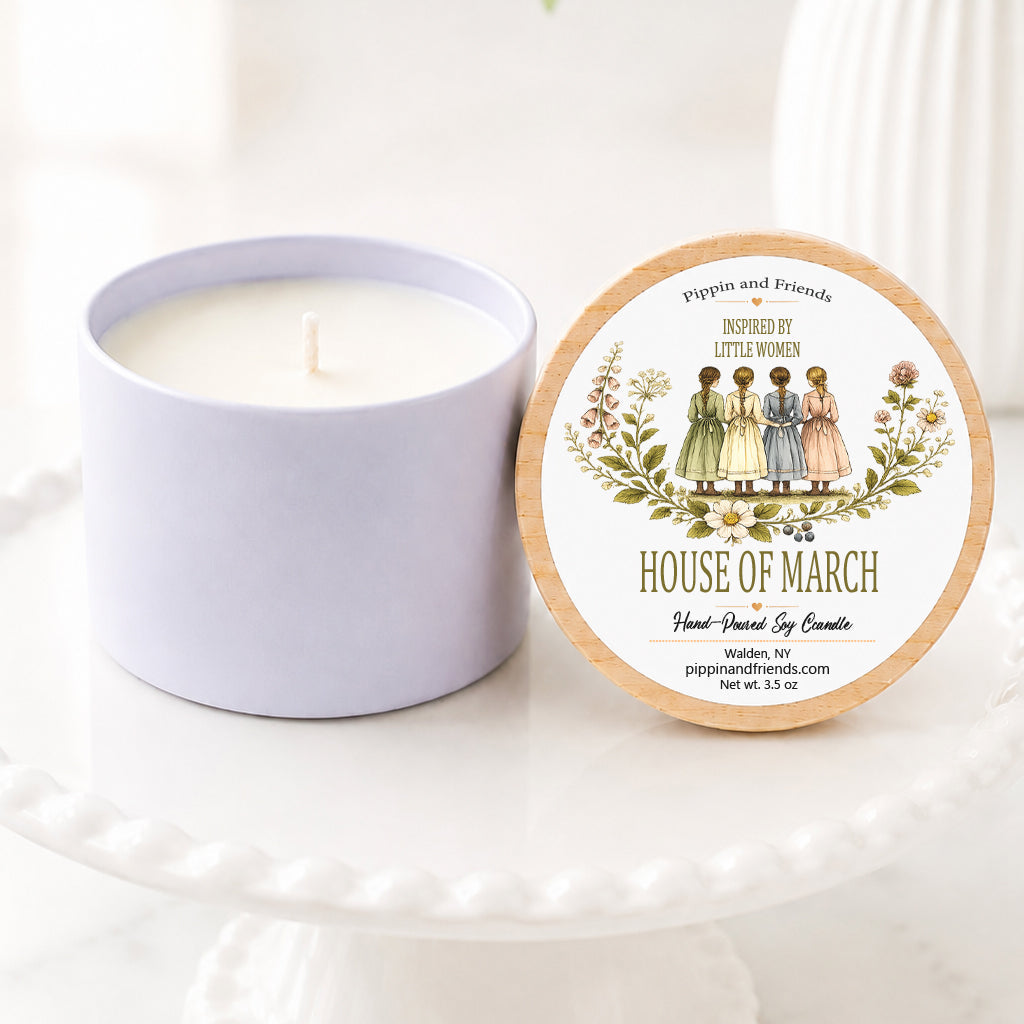 a hand-poured soy candle sits on a white scalloped pedestal beside its matching wooden lid. The lid features a Little Women–inspired label with a vintage watercolor illustration of the four March sisters standing together, framed by delicate wildflowers. The label reads "Inspired by Little Women – House of March" with "Hand-Poured Soy Candle" below. The candle is styled on a bright marble surface with a softly blurred white vase of flowers in the background, creating a warm look