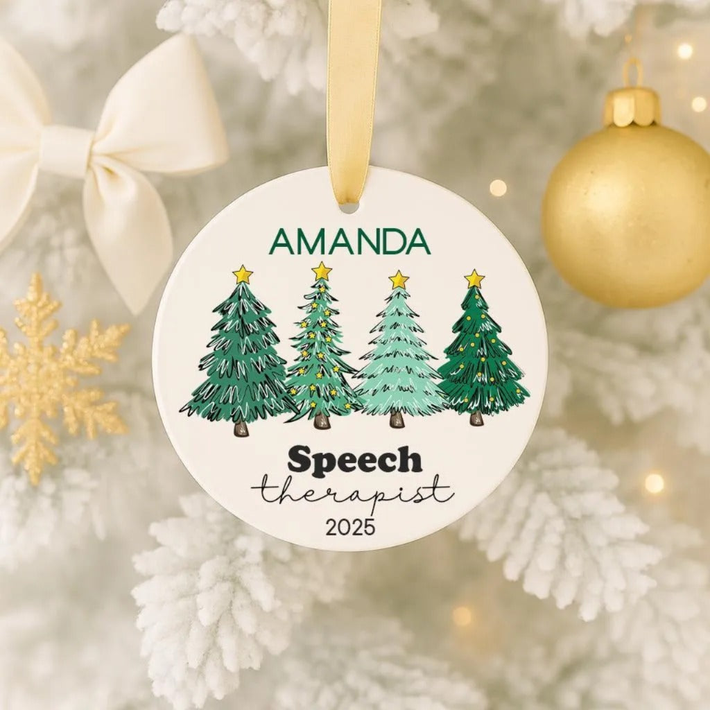 A white ornament with a gold ribbon, featuring a design of four green Christmas trees with stars, and the name "Amanda" and "Speech Therapist" written on it.