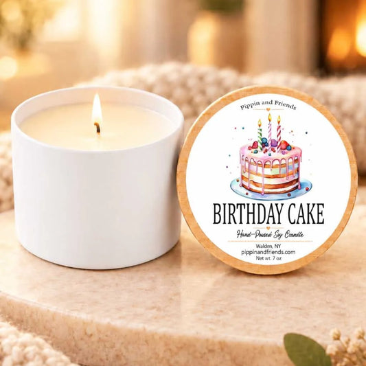 a white candle with a birthday cake design on it, placed on a wooden surface next to a white candle holder.