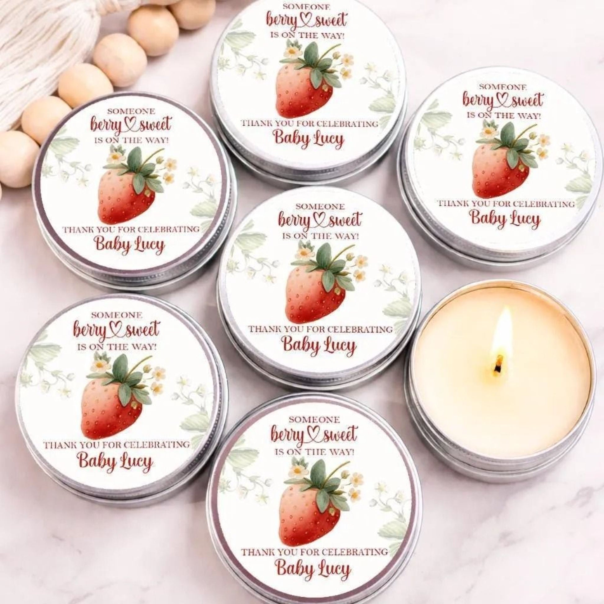 Strawberry baby shower candle favor with “Berry Sweet” personalized label in silver tin displayed on wooden surface.