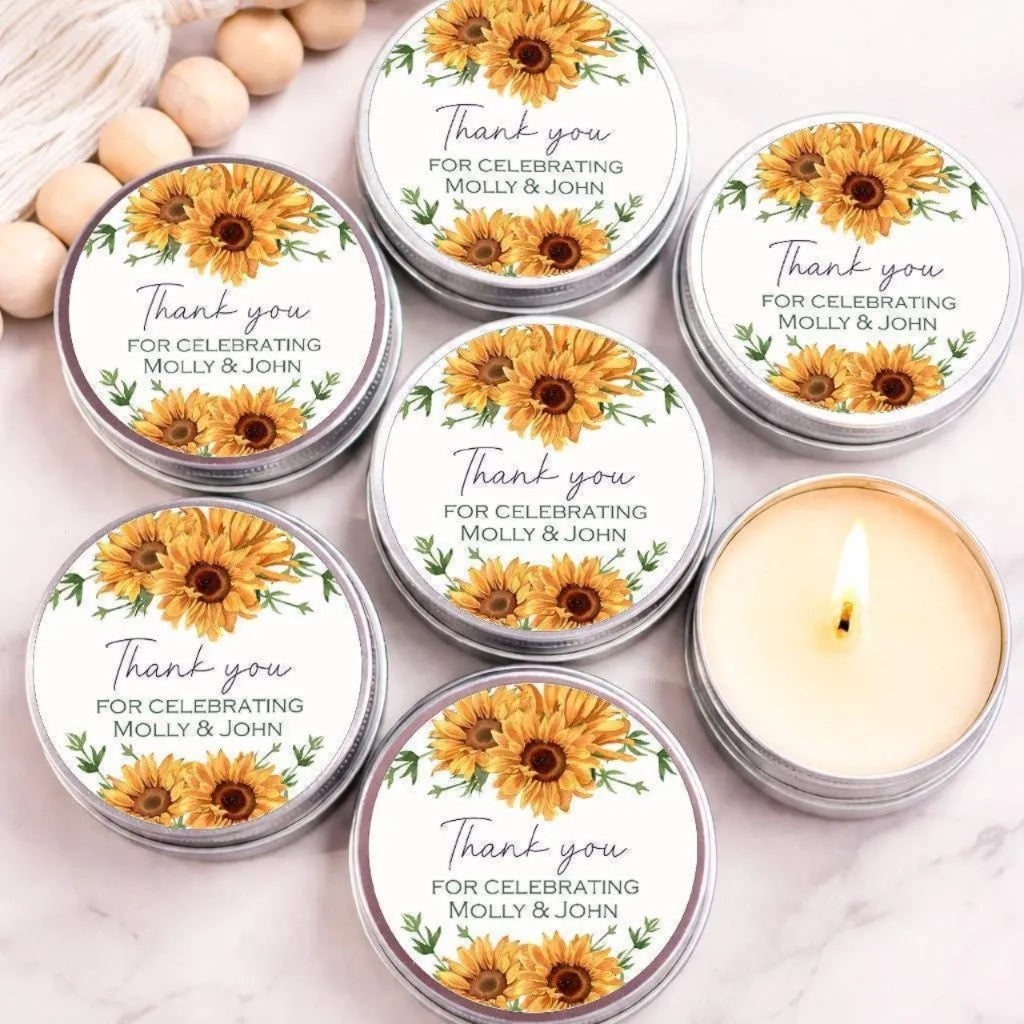a collection of round tin candles with a floral design, arranged on a marble surface. The candles are labeled with a message that reads "Thank you for celebrating Molly & John".