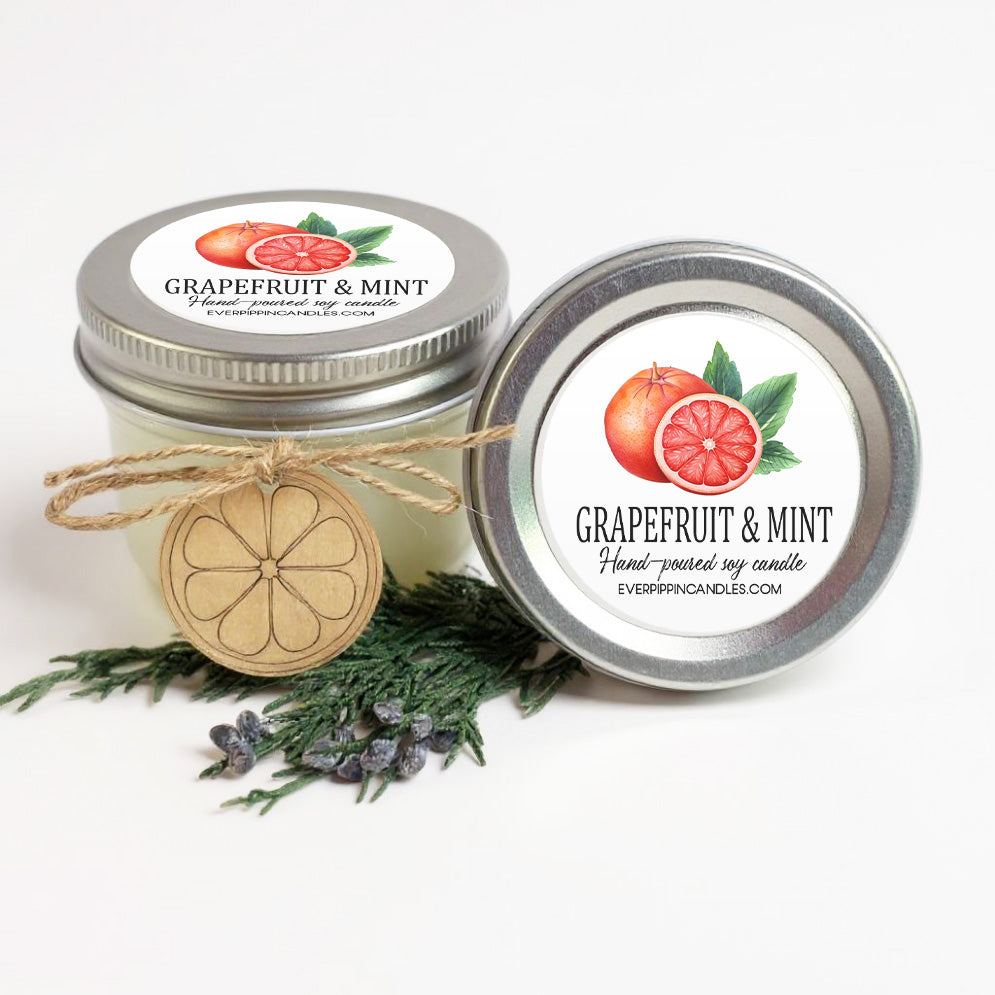two jars of grapefruit and mint scented candles, with a wooden tag and some greenery in the foreground.