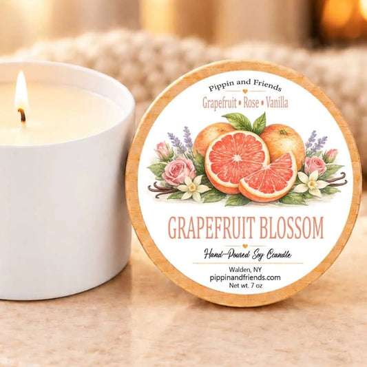 A white candle with a label that reads "Grapefruit Blossom" next to a lit candle on a table.