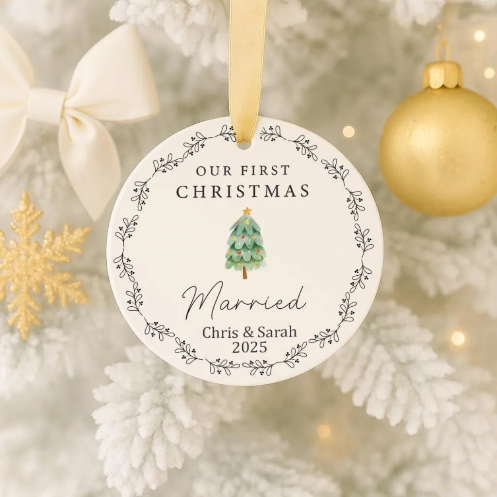 A white Christmas ornament with a gold ribbon and a small Christmas tree, hanging on a tree.