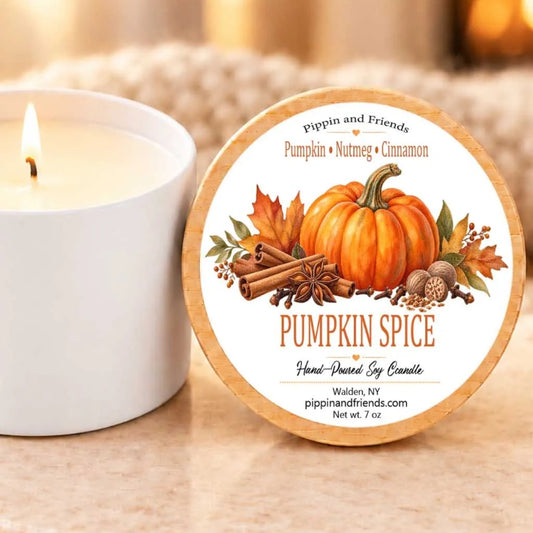 A white candle with a pumpkin and cinnamon label next to it, placed on a table.