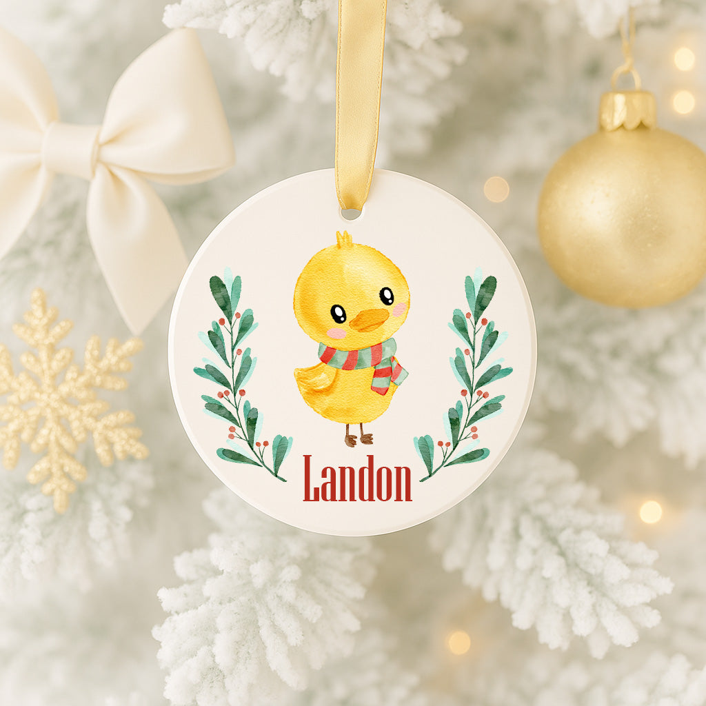 A white ornament with a yellow duck and green leaves, hanging on a Christmas tree.