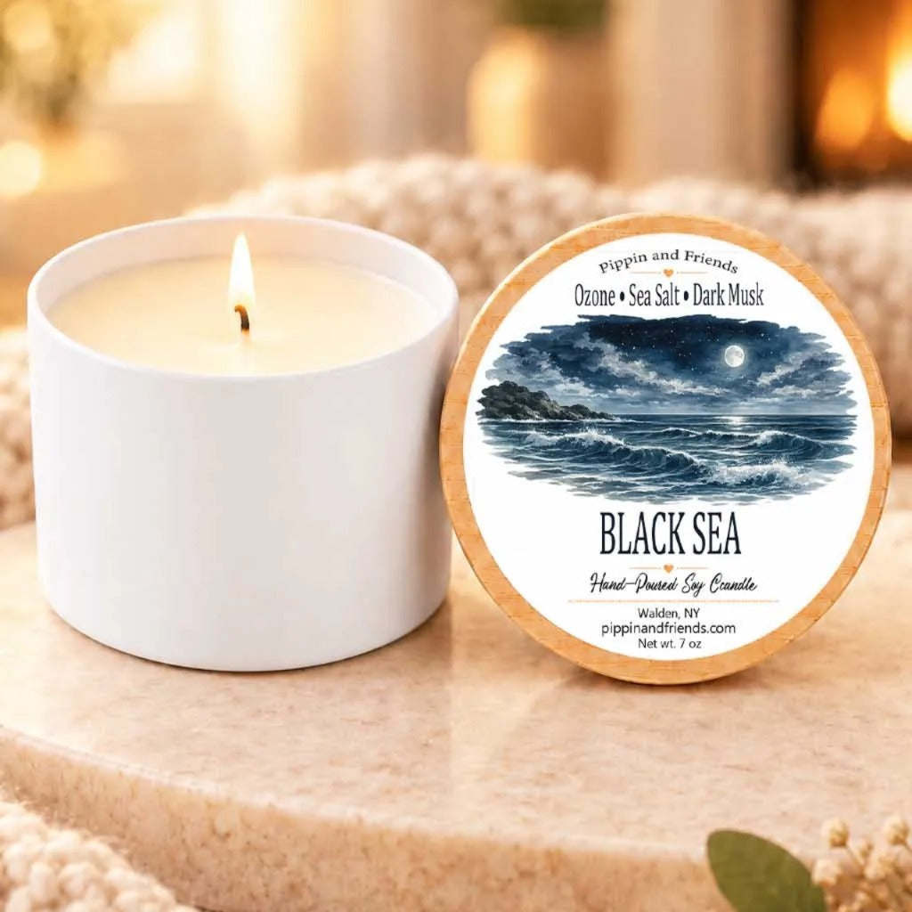 a white candle with a label that reads "Black Sea" and "Pippin and Friends" on a wooden surface.