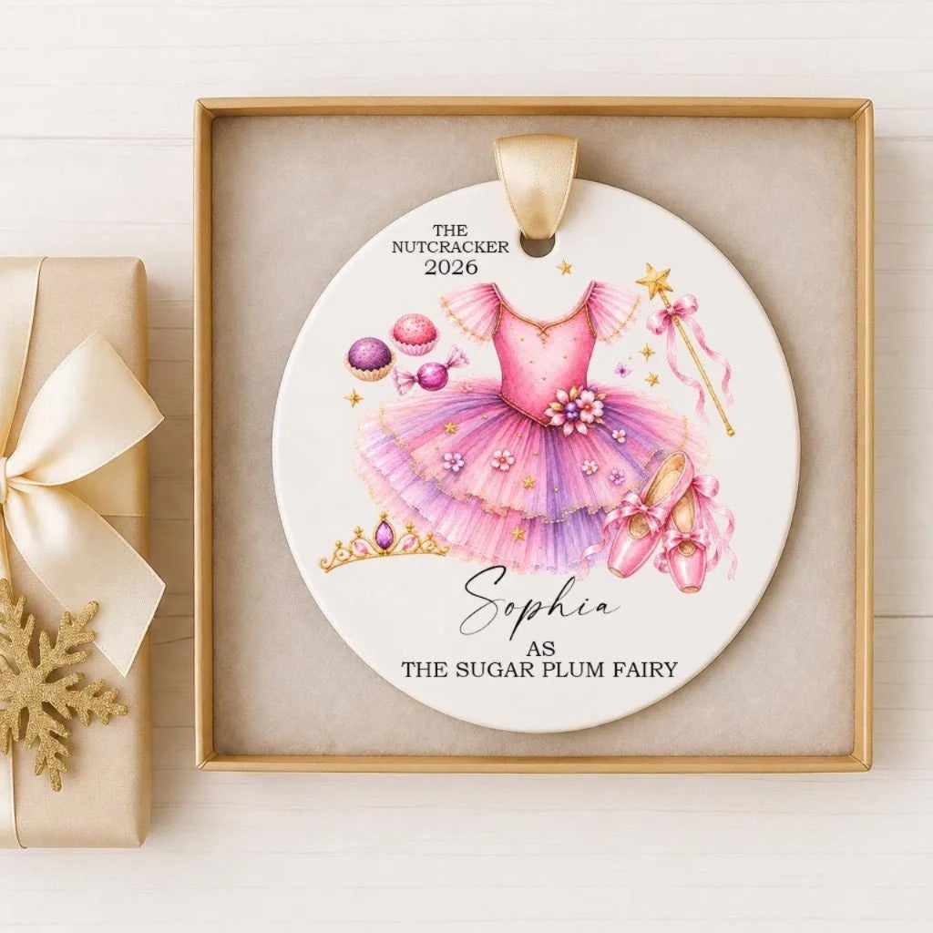 A decorative ornament featuring a pink tutu and ballet slippers, along with other ballet-related elements, such as a tiara and flowers, is displayed in a gold frame.