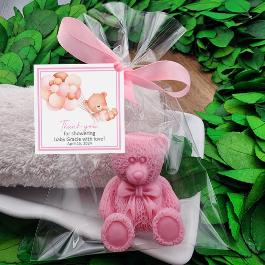 a pink teddy bear sitting on top of a white pillow