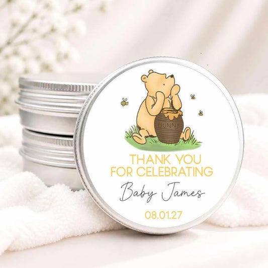 A round tin lid with a Winnie the Pooh-themed design, featuring a honey pot and the character Winnie the Pooh. The lid has text that says "Thank you for celebrating Baby James 08.01.27".