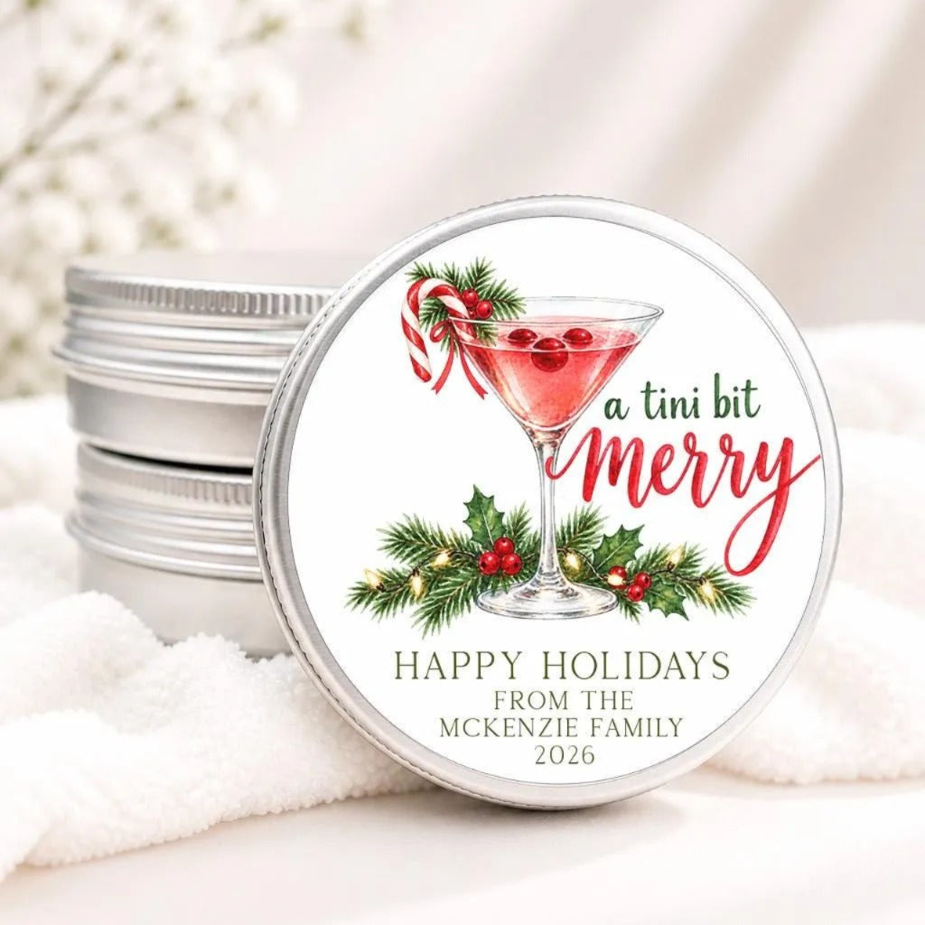 A round tin lid with a festive holiday design featuring a martini glass, holly leaves, and red berries, along with the text "a tini bit merry" and "Happy holidays from the McKenzie family 2026".