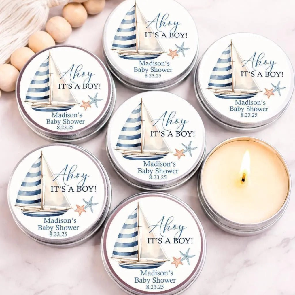a collection of six tin candles with the text "Ahey IT'S A BOY!" printed on them, along with the date and location of a Madison's Baby Shower. The candles are arranged on a marble surface, with a few wooden beads visible in the background.