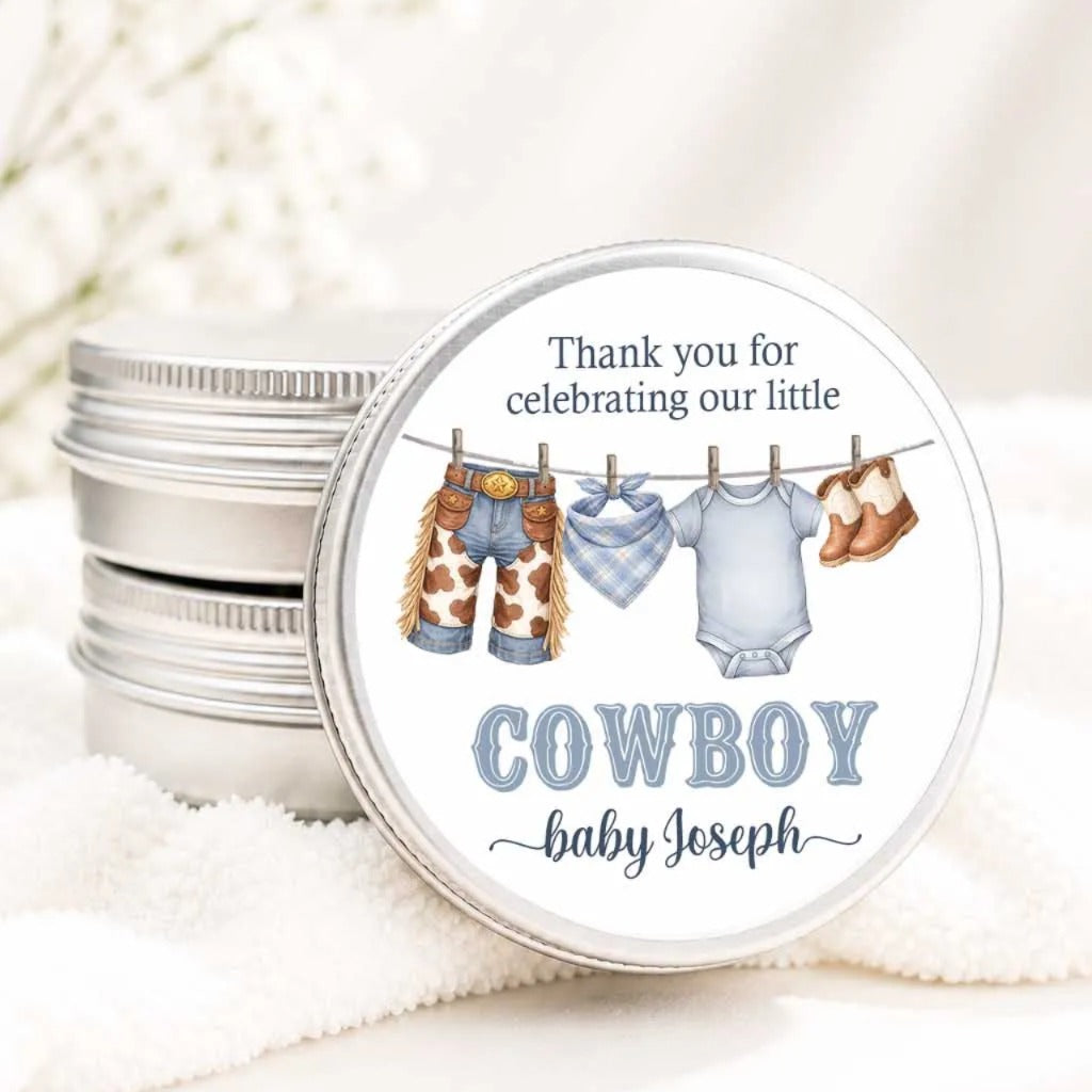 A round tin with a label that says "Thank you for celebrating our little COWBOY baby Joseph" and features illustrations of baby clothes and shoes hanging on a clothesline.