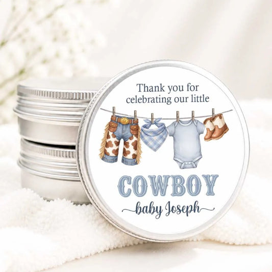 A round tin with a label that says "Thank you for celebrating our little COWBOY baby Joseph" and features illustrations of baby clothes and shoes hanging on a clothesline.