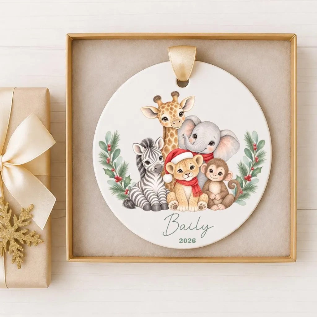 A decorative ornament featuring a group of animals, including a giraffe, zebra, lion, elephant, and monkey, all wearing Santa hats and surrounded by greenery. The ornament is displayed in a gold frame, and there is a gift box visible in the background.