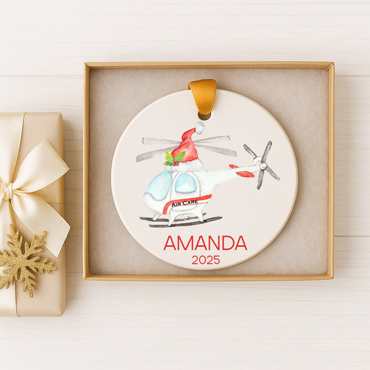 A ceramic ornament in the shape of a helicopter, with the name "Amanda" and the year "2025" printed on it, is displayed in a box.