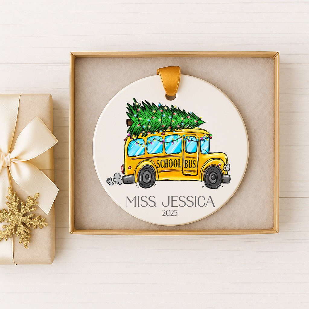 A ceramic ornament featuring a yellow school bus carrying a Christmas tree, with the name "Miss Jessica" and the year "2025" displayed below.
