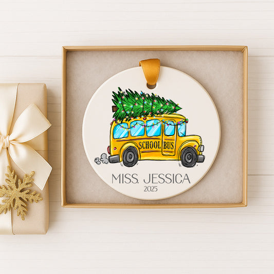 A ceramic ornament featuring a yellow school bus carrying a Christmas tree, with the name "Miss Jessica" and the year "2025" displayed below.