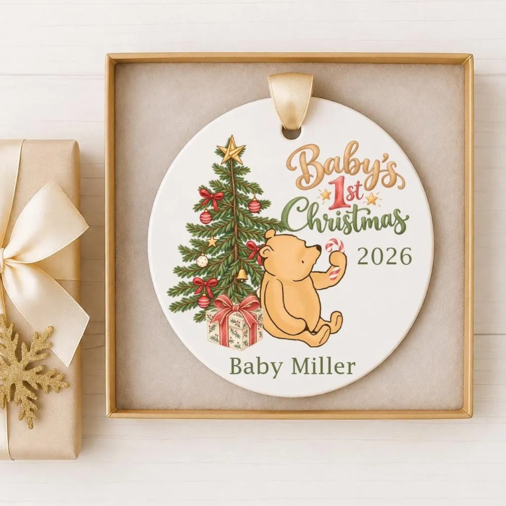 A white ceramic ornament with a gold frame, featuring a teddy bear and a Christmas tree. The ornament displays the text "Baby's 1st Christmas 2026" and "Baby Miller".