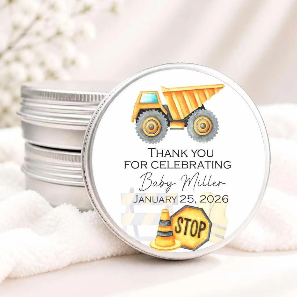a round tin lid with a label that says "Thank you for celebrating Baby Miller JANUARY 25, 2026" along with an illustration of a dump truck and a stop sign.