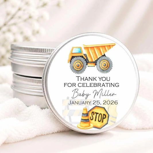 a round tin lid with a label that says "Thank you for celebrating Baby Miller JANUARY 25, 2026" along with an illustration of a dump truck and a stop sign.