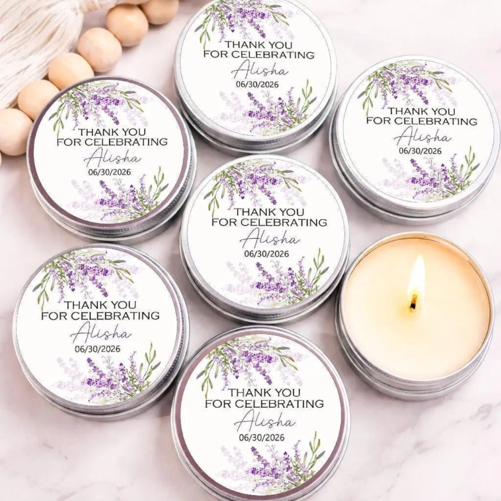 a collection of six silver tin candles with white labels, each featuring a floral design and personalized text. The candles are arranged on a marble surface, with some of them lit, creating a warm and inviting atmosphere.