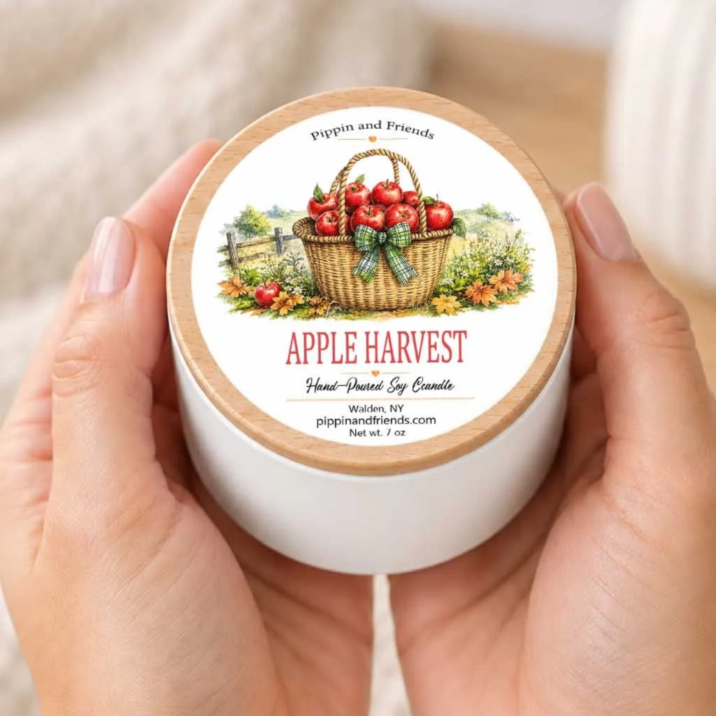 A person's hands holding a white container with a label featuring an illustration of a basket filled with apples, surrounded by a countryside scene.