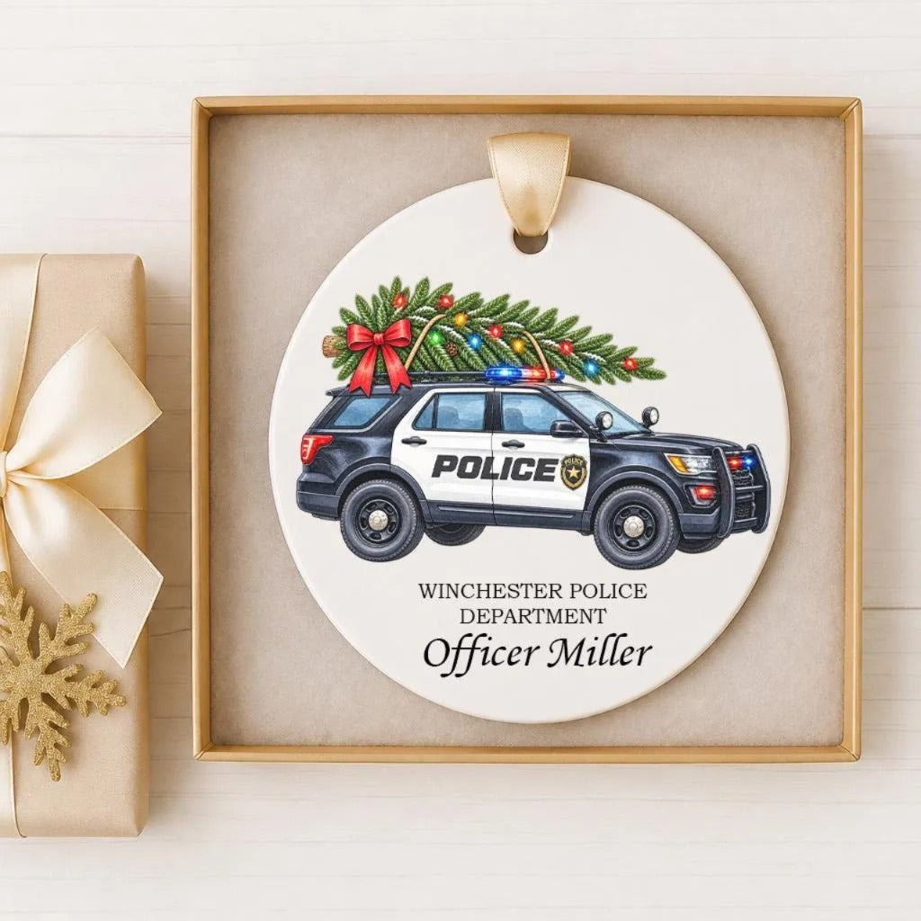 A white ceramic ornament featuring a police car with a Christmas tree on top, displayed in a wooden frame.