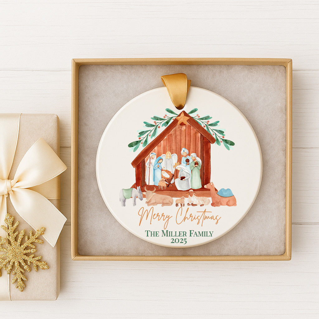 A white ornament with a Christmas nativity scene and the text "Merry Christmas The Miller Family 2020" is displayed in a gold frame on a white wooden surface.