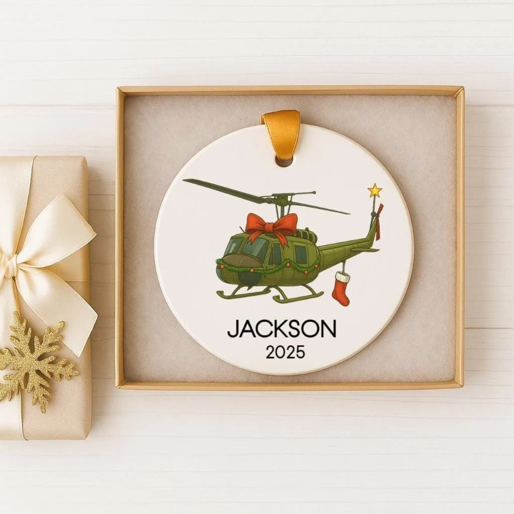 A ceramic ornament featuring a green helicopter with a red bow, displayed in a wooden box.