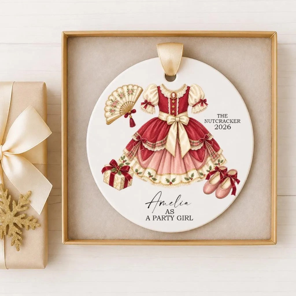 A decorative ornament featuring a red and gold dress, a fan, and a gift box, with the text "The Nutcracker 2026" and "Amelia as a Party Girl" printed on it.