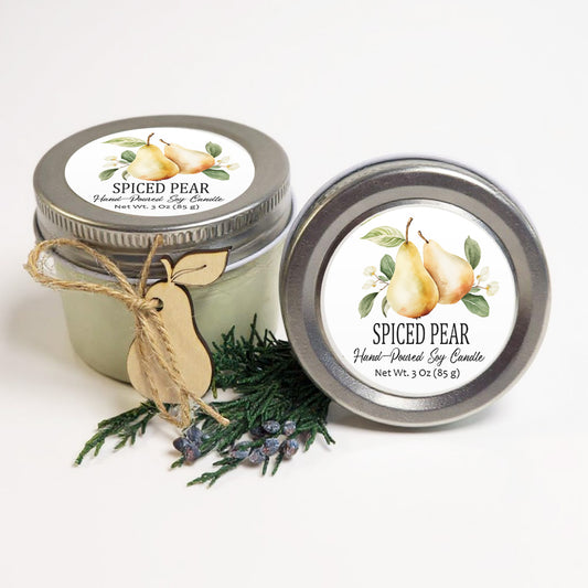 two jars of SPICED PEAR hand-poured soy candle, with a wooden tag and pine branches in the foreground.