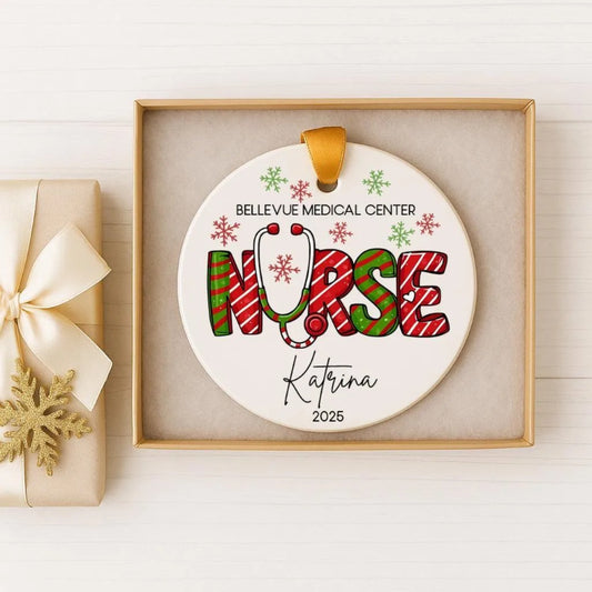 A white ceramic ornament with the word "NURSE" written on it, decorated with snowflakes and a stethoscope, placed inside a gold box.