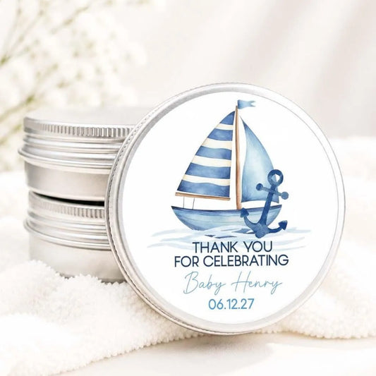 A round tin lid with a blue and white sailboat illustration and a message that says "Thank you for celebrating Baby Henry 06.12.27".