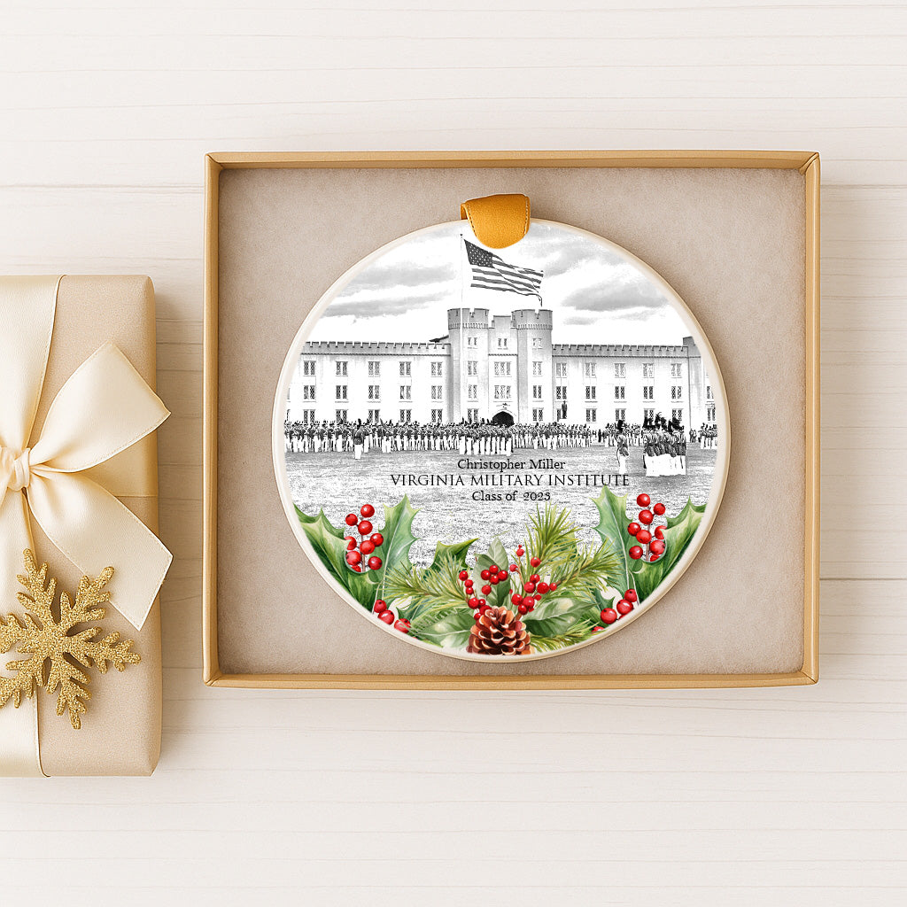 A decorative ornament featuring a black and white illustration of the Virginia Military Institute, with a flag and holly leaves, displayed in a gold frame.
