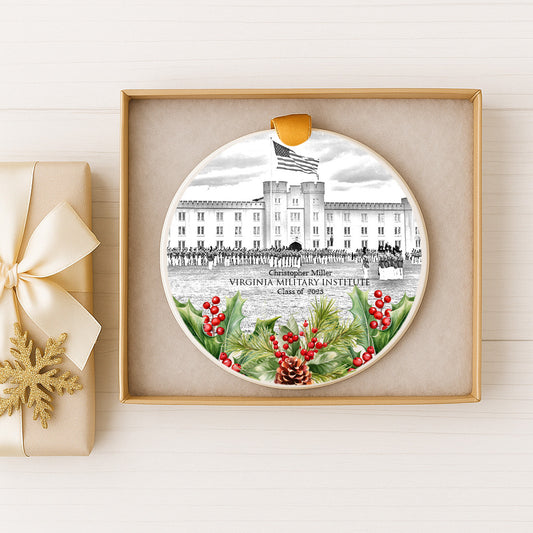 A decorative ornament featuring a black and white illustration of the Virginia Military Institute, with a flag and holly leaves, displayed in a gold frame.