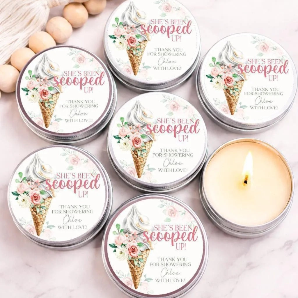 a collection of six round tin containers with a floral design, each containing a scoops of ice cream and a candle. The containers are arranged on a marble surface, with a lit candle in one of them.